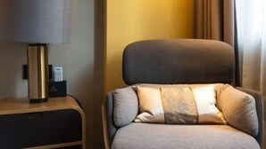 A hotel room with a grey armchair, a lamp, and a remote control on a wooden side table. - Joyous Hotel (Shanghai)