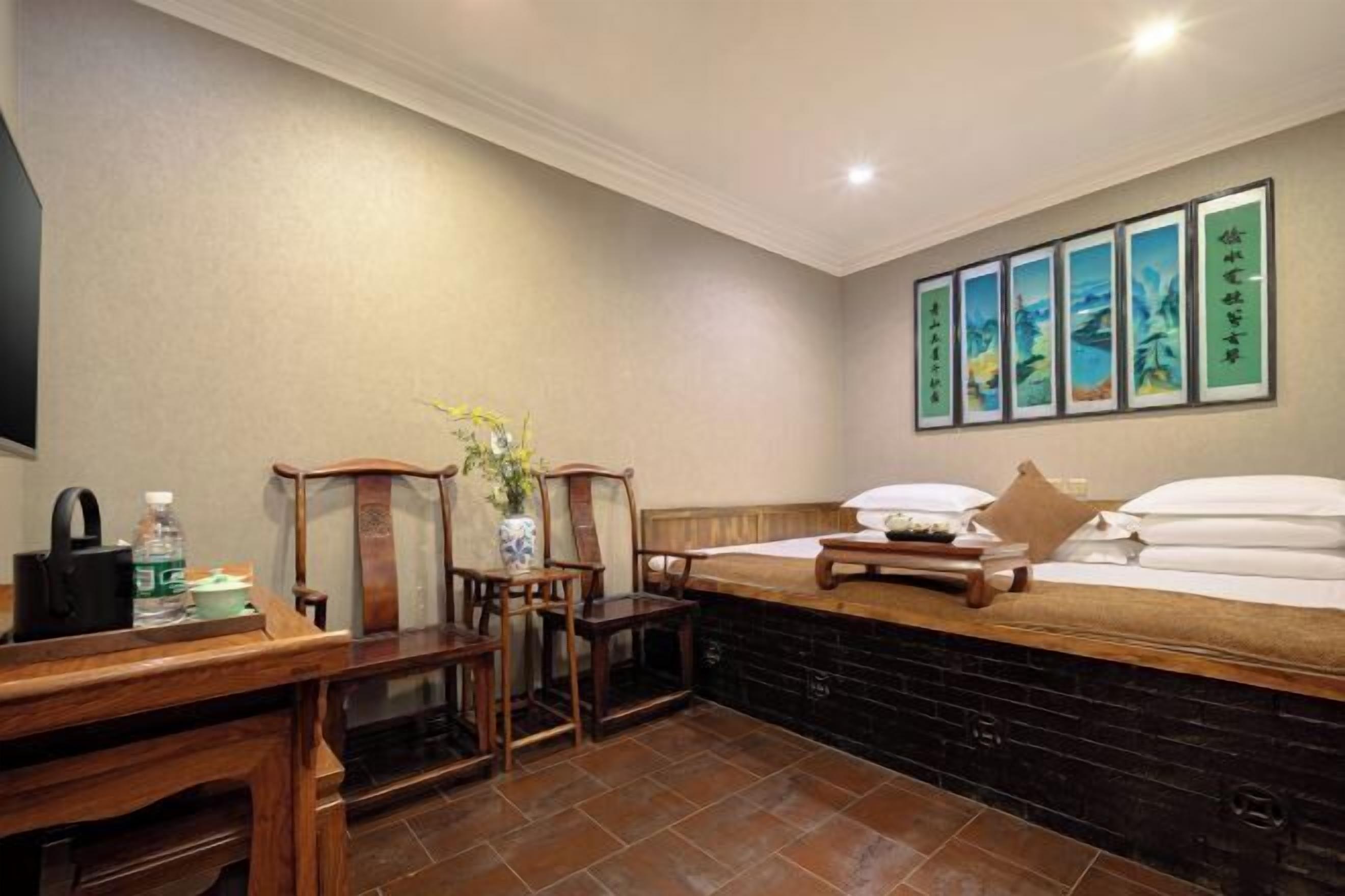 A hotel room with a bed, a desk, chairs, a vase with flowers, and artwork on the wall.