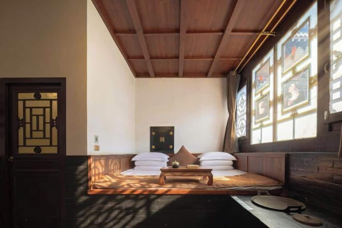 A traditional Japanese-style room with tatami flooring, a low wooden bed, a small table, and a sliding door.