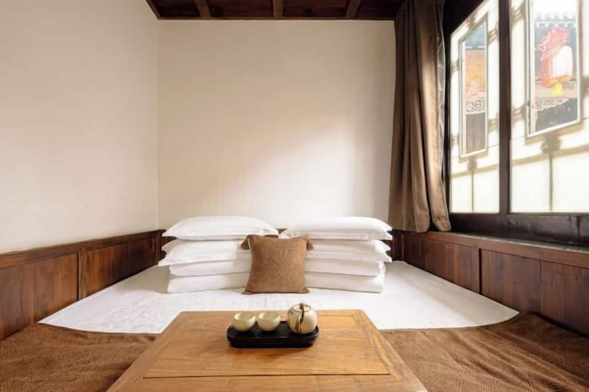 A room with a bed, pillows, a tray with cups, and a window with curtains.