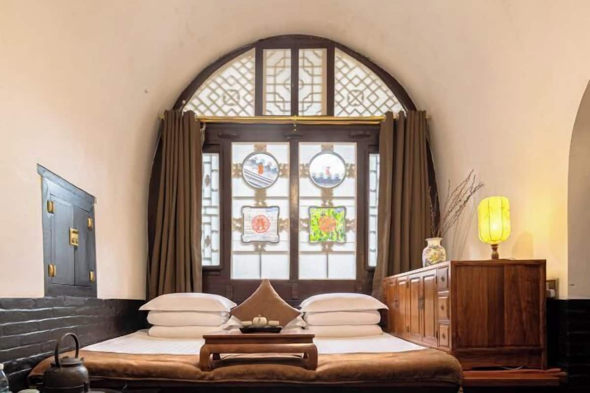 A traditional room with a bed, a wooden cabinet, a tea kettle, and a window with decorative glass panels.