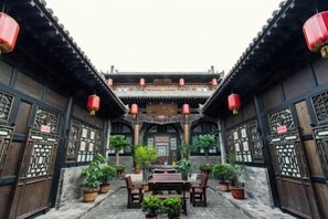 A traditional courtyard with a wooden table and chairs, potted plants, and red lanterns.