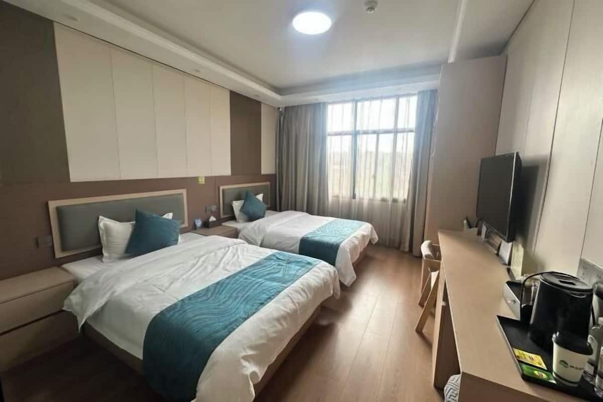 A hotel room with two beds, a desk with a coffee maker, a TV, and a window with curtains.