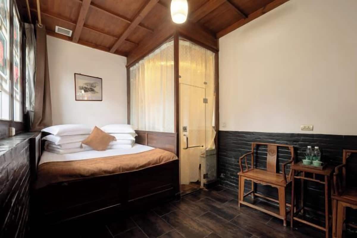 A bedroom with a bed, a wooden chair, a small table, and a door leading to a bathroom.