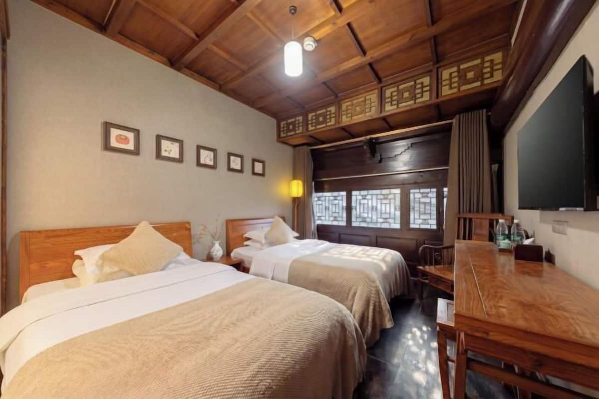 A hotel room with two beds, a wooden ceiling, a desk, and a TV.