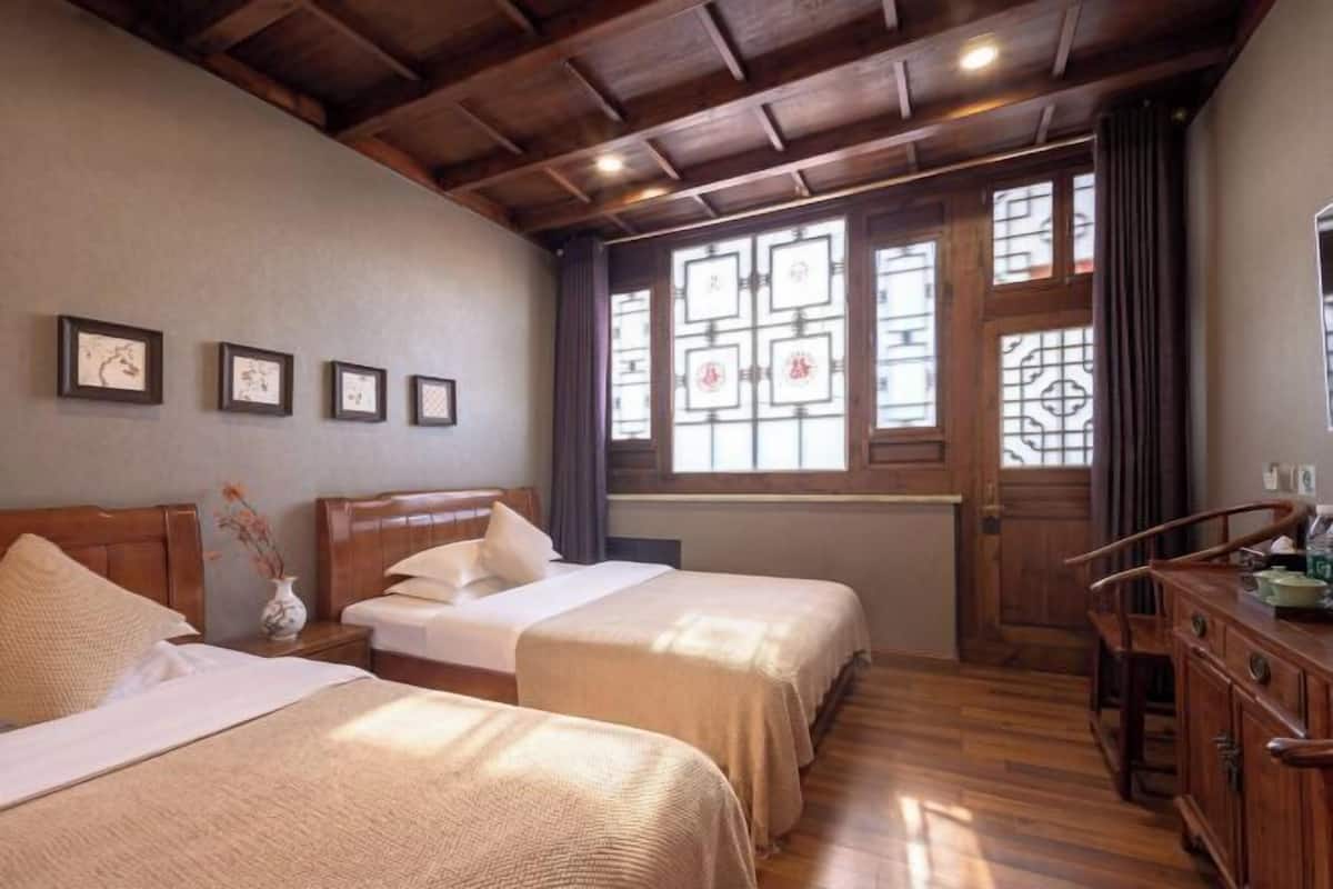 A room with two beds, wooden headboards, a wooden cabinet, and a window with decorative glass panes.