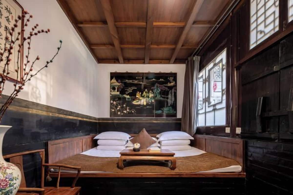 A traditional room with a bed, pillows, a small table, and a window with a view.