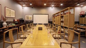 Un salón de conferencias con una larga mesa de madera, sillas, una pantalla de proyector y estanterías de madera.
