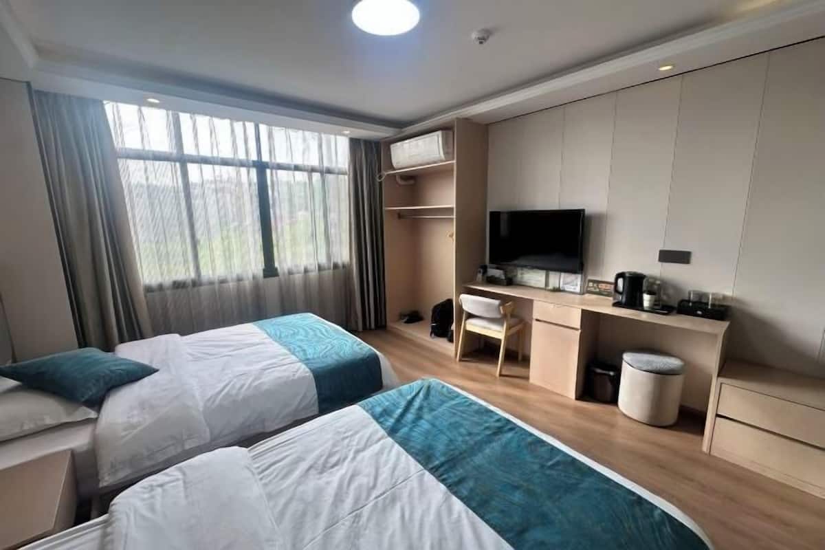 A hotel room with two beds, a desk, a TV, and a window with curtains.