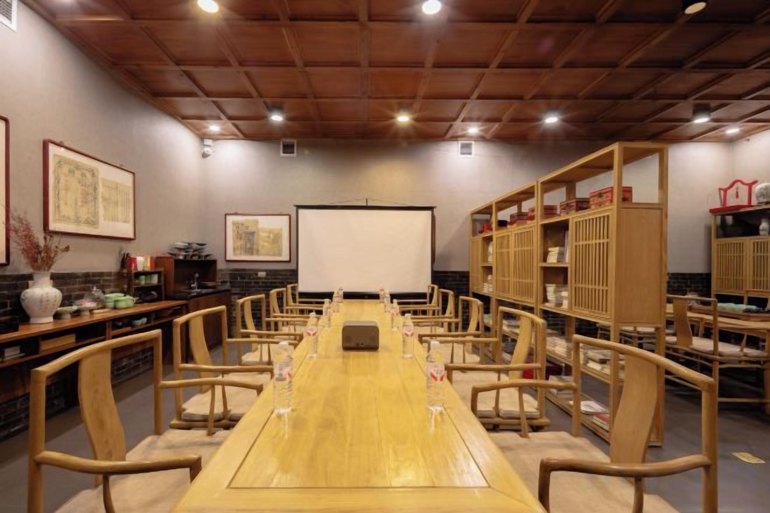 Une salle de conférence équipée d’une longue table, de chaises, d’un écran de projection et d’étagères en bois.