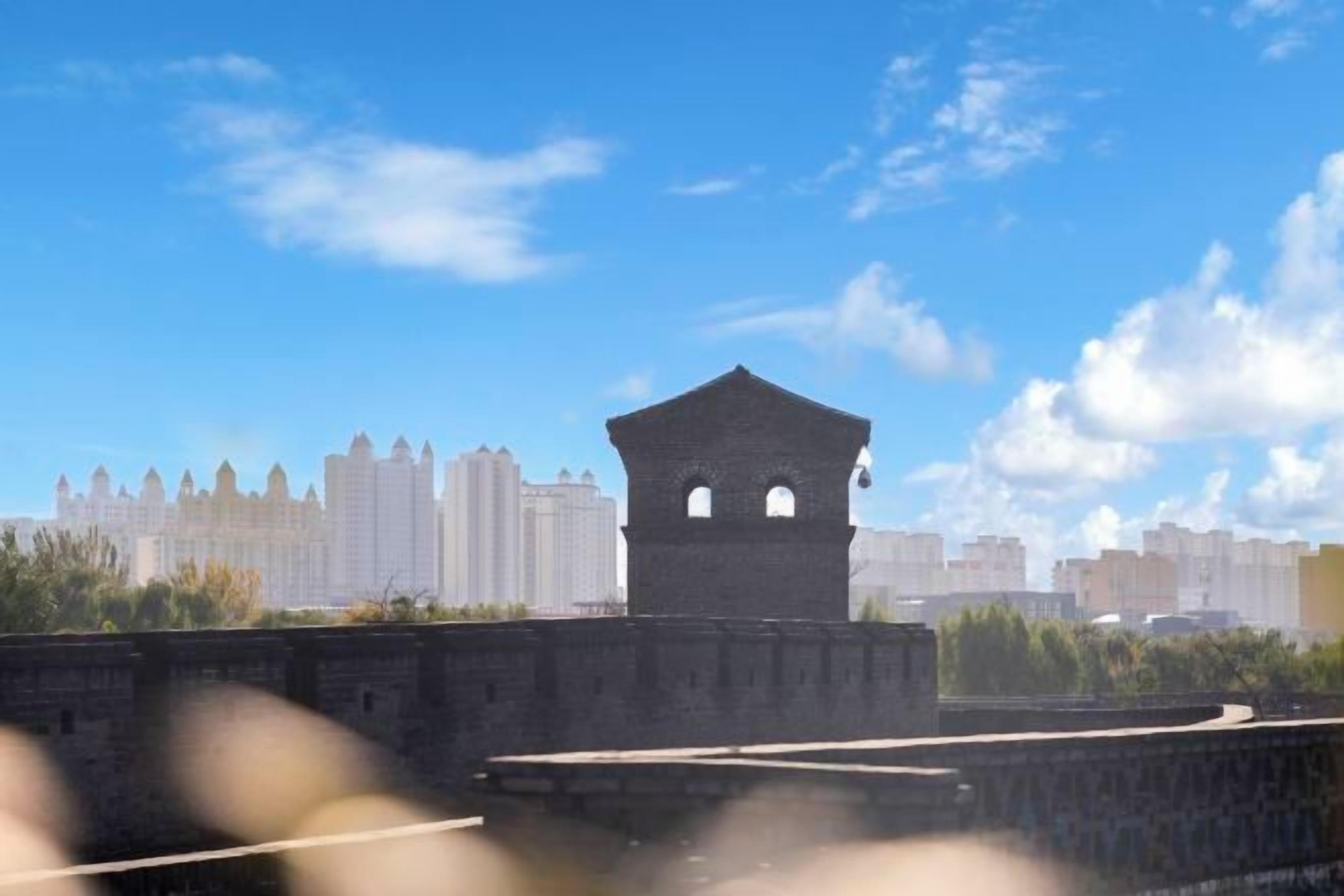 Une tour historique, dotée d’une toiture plate et d’ouvertures en arc, qui surplombe un paysage urbain moderne avec ses nombreux immeubles de grande hauteur.