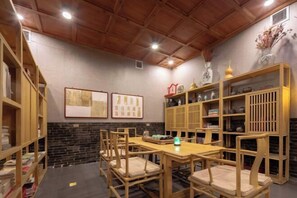 A room with a wooden ceiling, a brick wall, a wooden table with chairs, and shelves with books and decorative items. - Jing Xiu Wudedi Cultural Hall (Pingyao County)