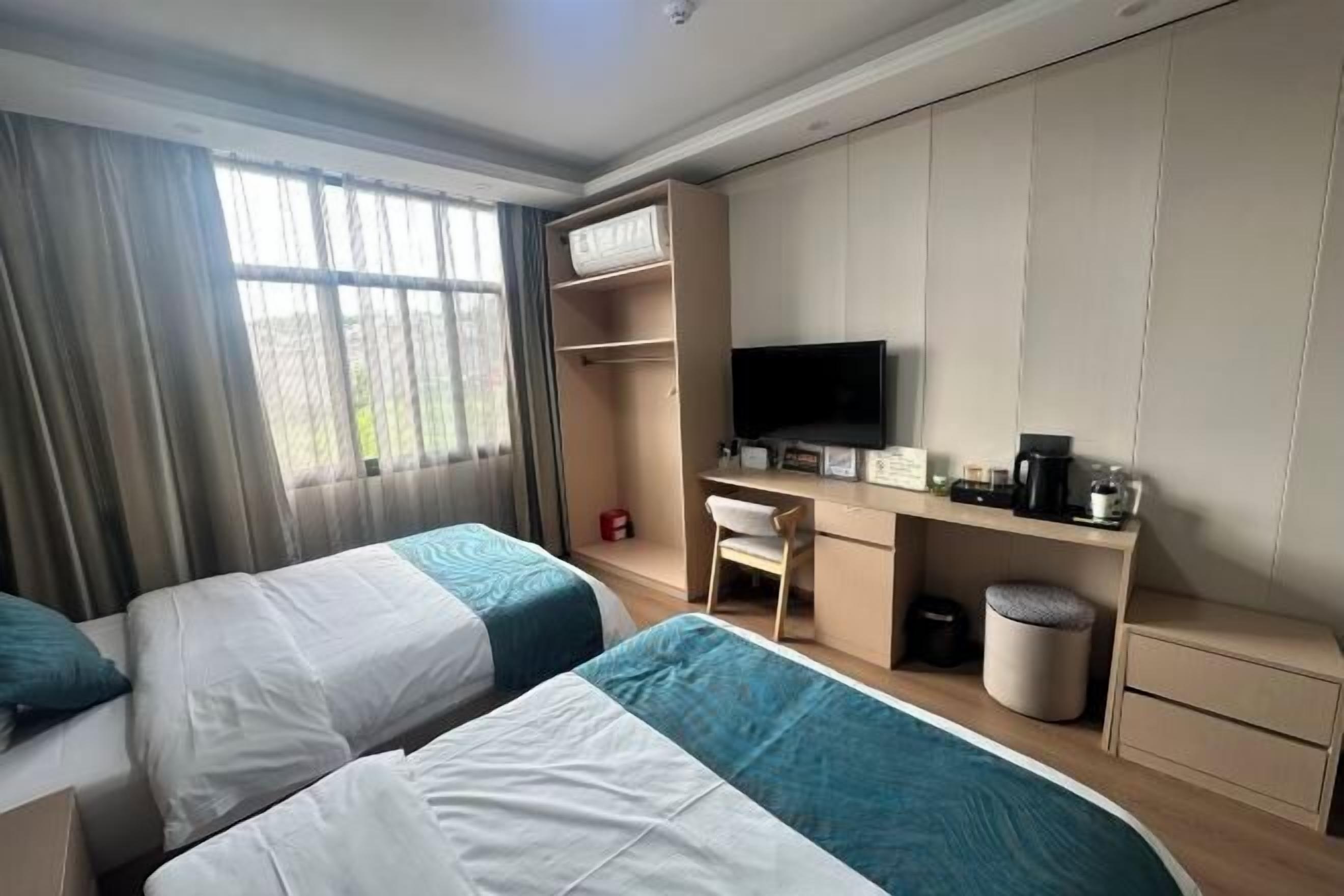 A hotel room with two beds, a desk, a TV, and a window with curtains.