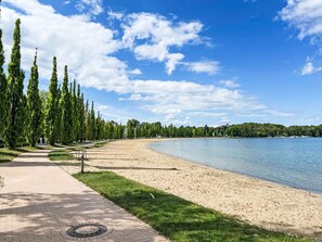 Een verhard pad langs een zandstrand, met een helder uitzicht op het water en verafgelegen bomen.