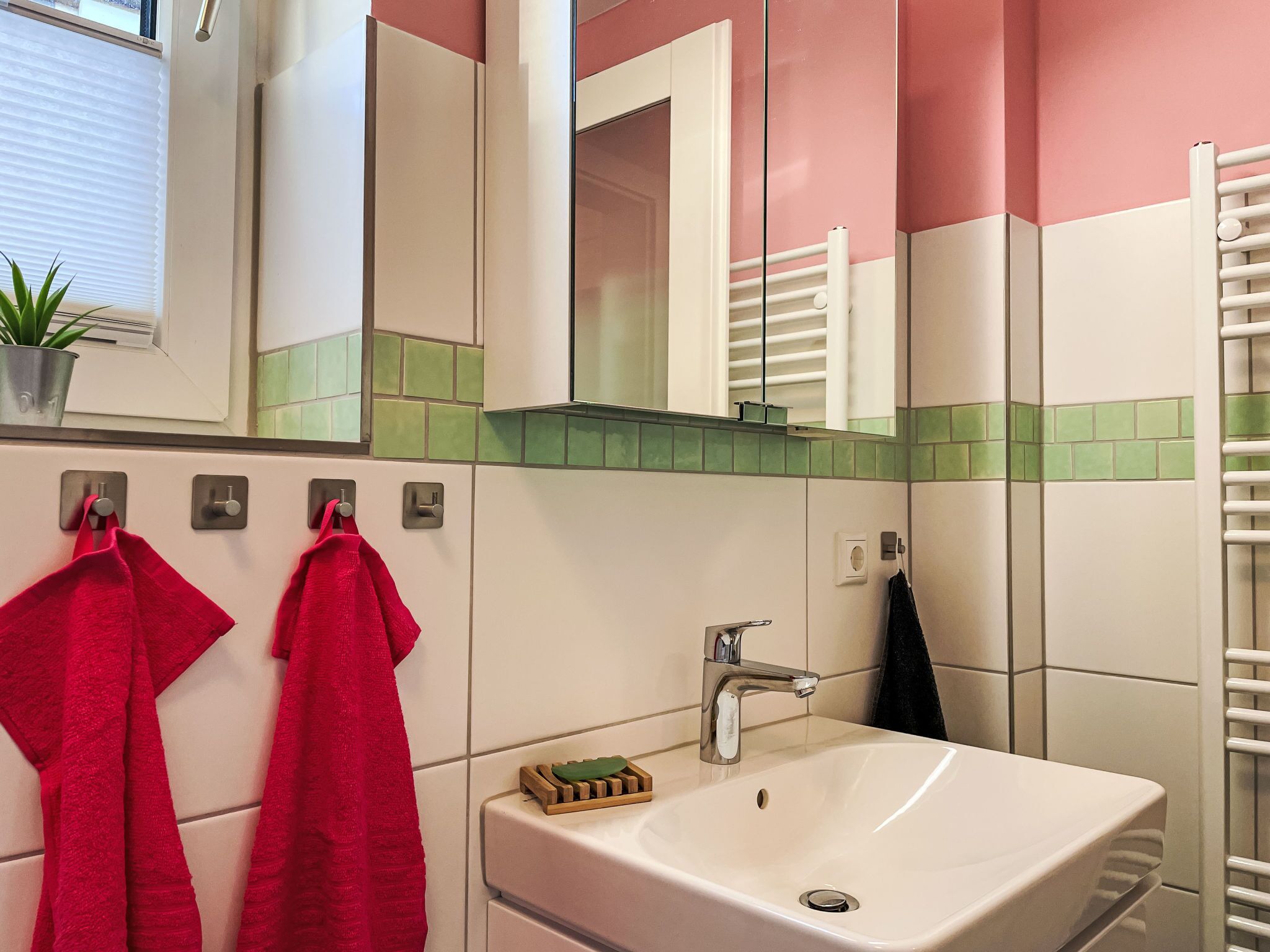 A bathroom with a white sink, a mirror, and two red towels hanging on hooks.