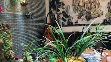 A room with a brick wall, a large painting, and various potted plants.