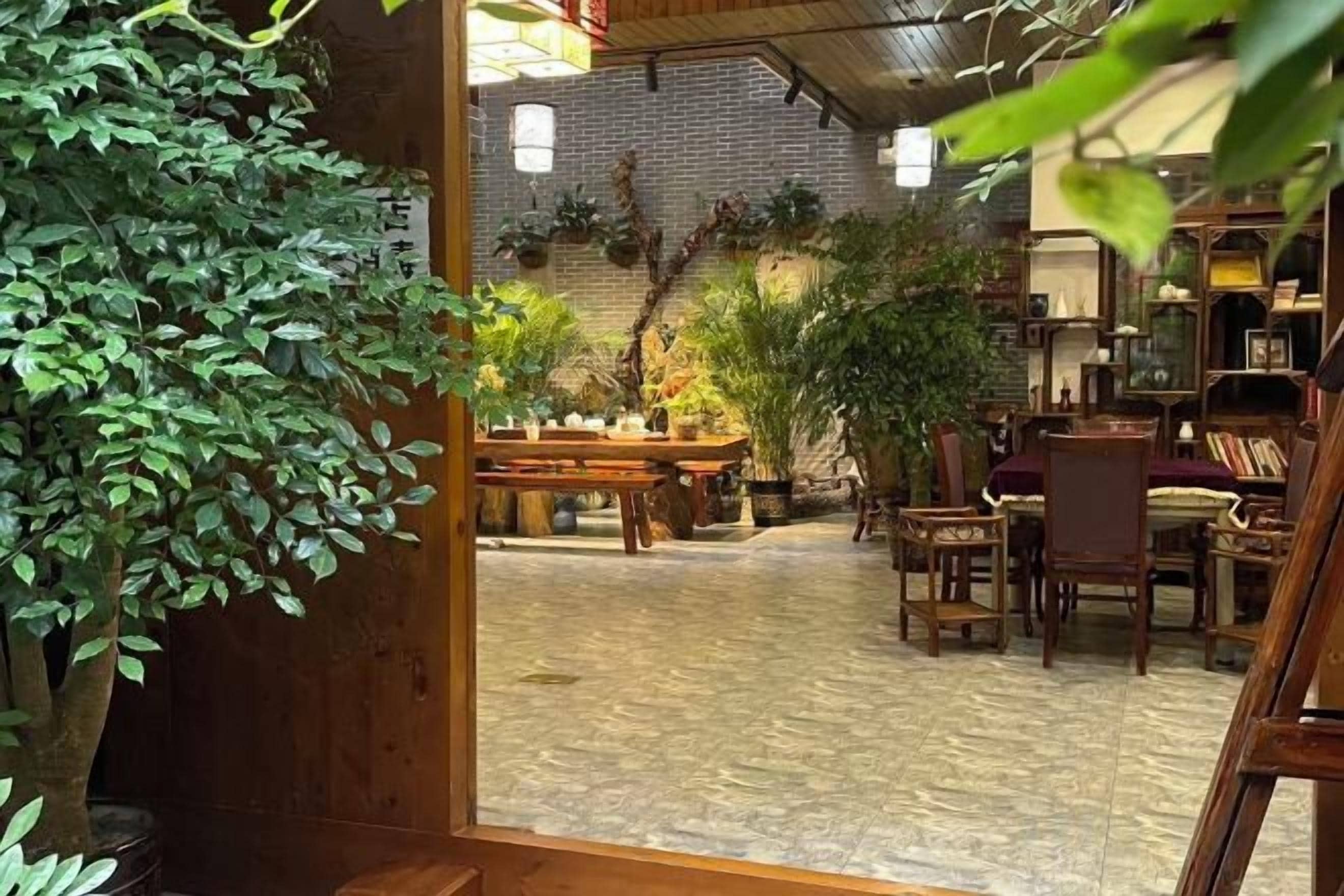 Un espacio interior con piso de madera, mesas, sillas y plantas en macetas.
