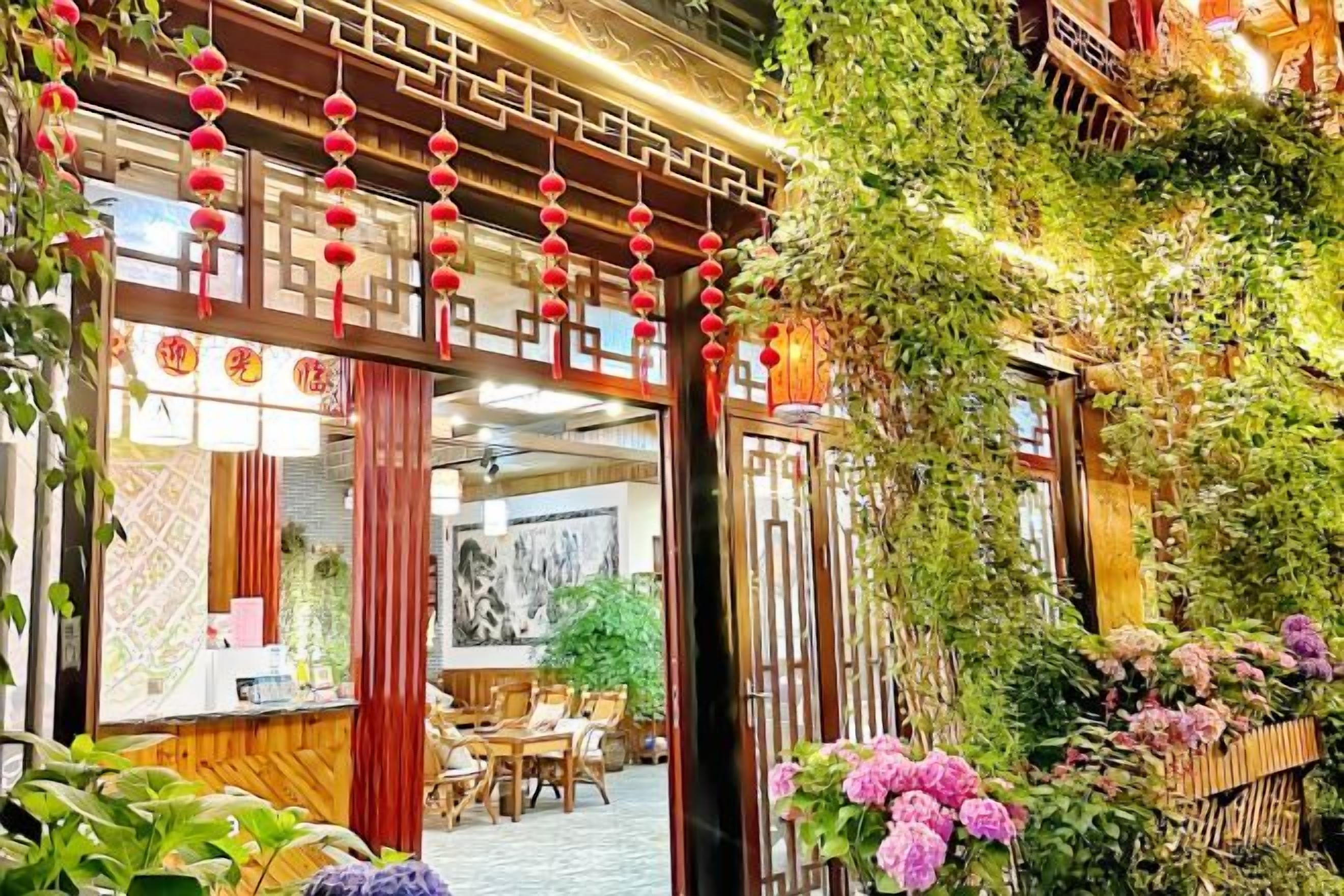 A traditional Chinese courtyard with a wooden gate, red lanterns, and lush greenery.