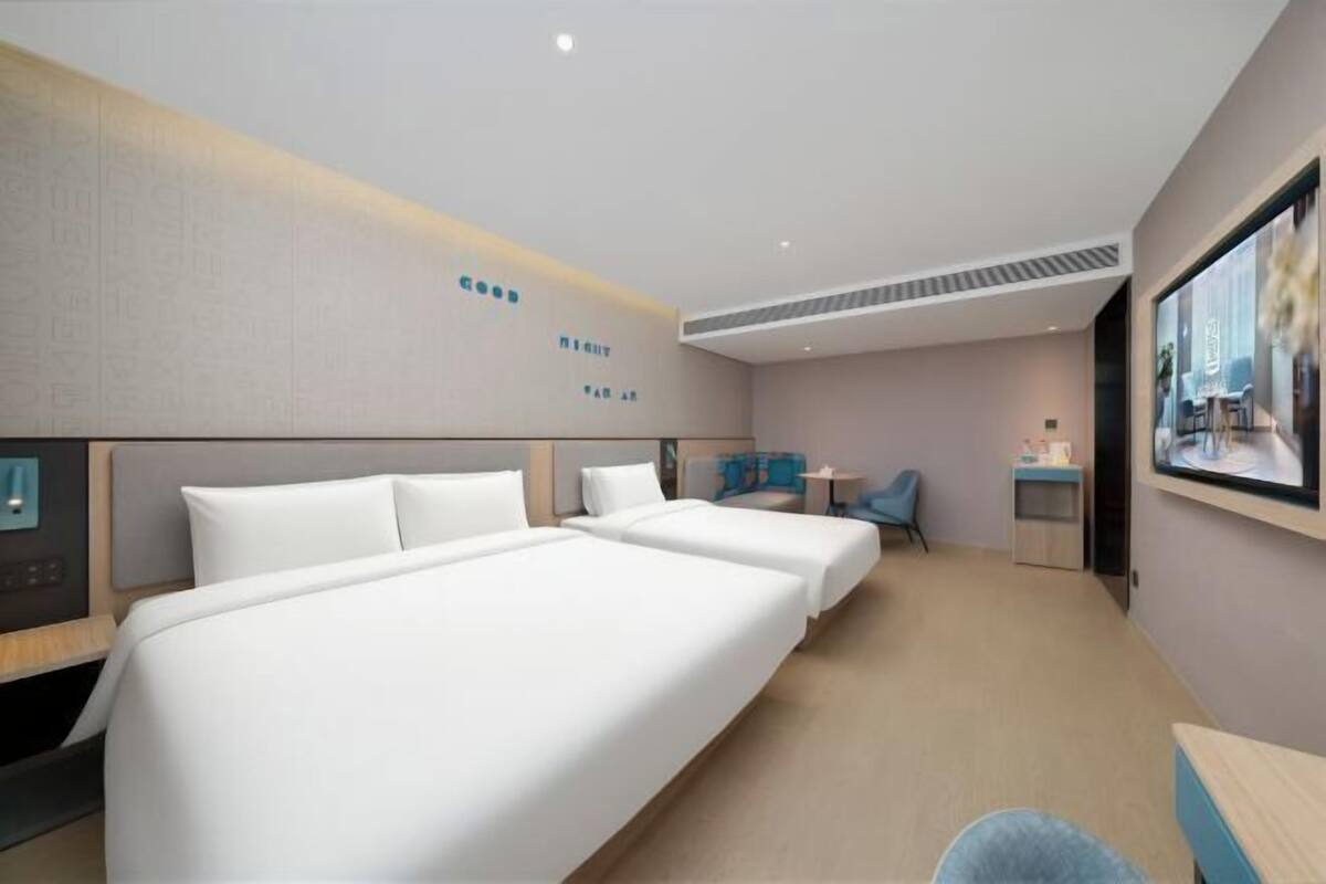 A hotel room with two beds, a desk, a chair, a TV, and a wall-mounted artwork.