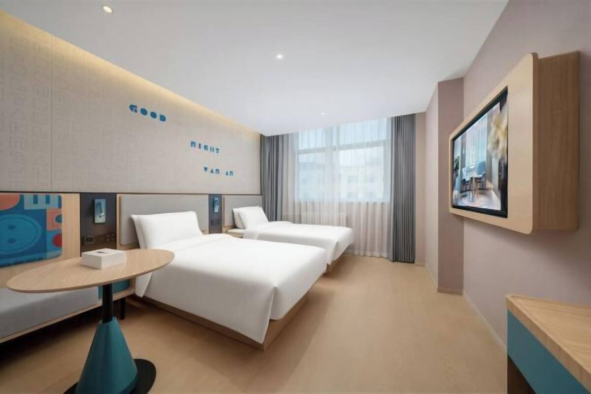 A hotel room with two beds, a small table, a TV, and a window with curtains.