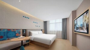 A modern hotel room with a bed, a seating area, a small table, and a large window with curtains.