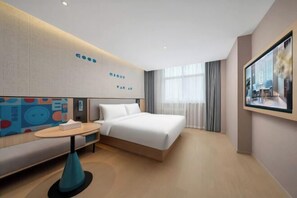 A modern hotel room with a bed, a seating area, a small table, and a large window with curtains.
