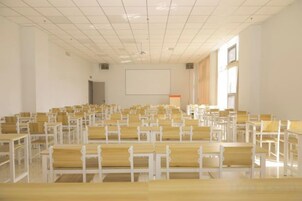 Un auditorio con filas de sillas y mesas de madera, una pantalla de proyector y un ventanal grande.