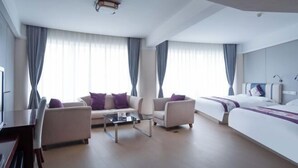 Una habitación de hotel moderna con sofá, sillones, una mesa de centro, cama y televisión.