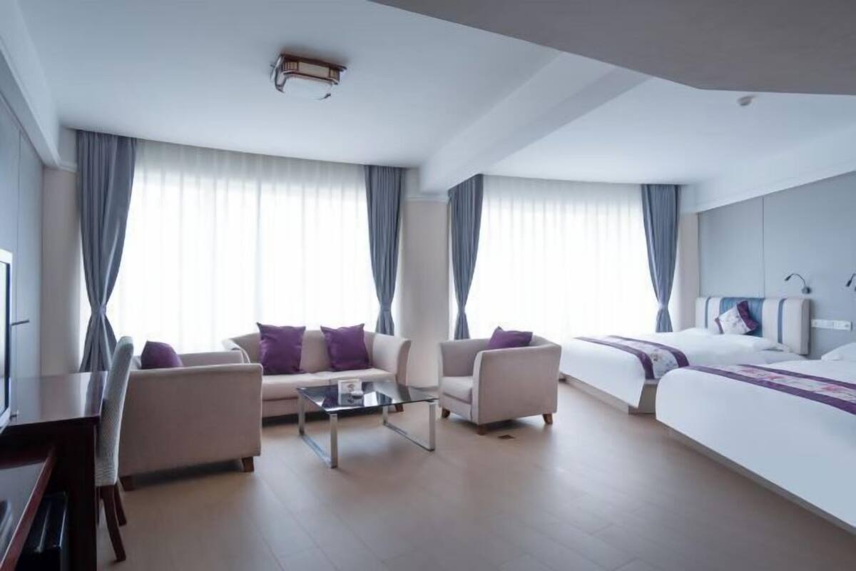 A modern hotel room with a sofa, armchairs, a coffee table, a bed, and a TV.