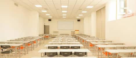 A classroom with rows of tables and chairs, a projector screen, and a whiteboard.