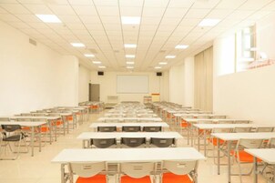 Un aula con filas de mesas y sillas, una pantalla de proyector y una pizarra.