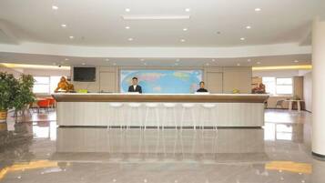 A reception area with a counter, two staff members, a large screen, and a seating area with chairs.