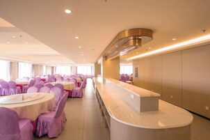 A hotel dining area with round tables, purple chair covers, a long counter, and a modern ceiling design.