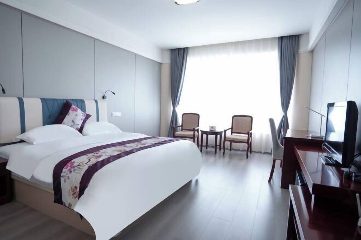 A hotel room with a bed, a desk, a TV, and a seating area with chairs.