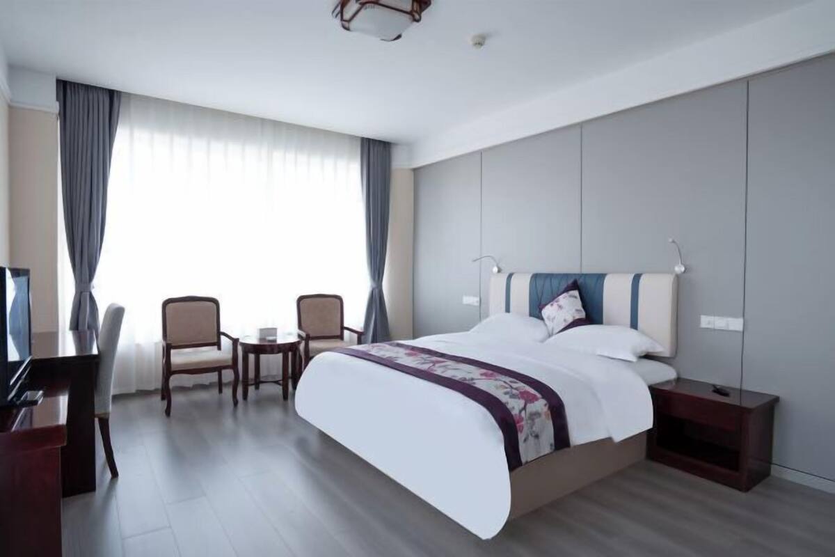 A hotel room with a bed, a desk, a chair, a small table, and a nightstand.