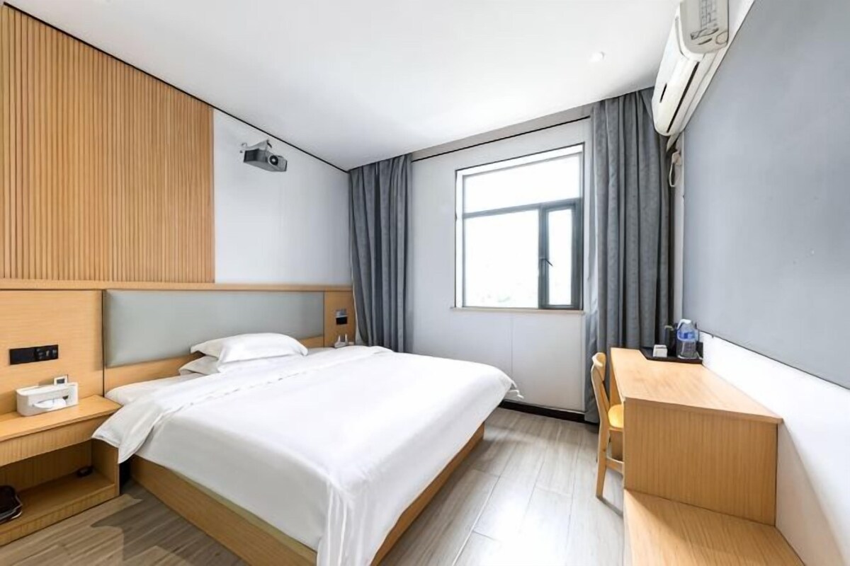 A hotel room with a bed, bedside table, desk, and a window with curtains.