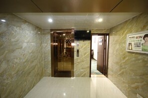 A hotel lobby with a marble wall, a reception desk, and a poster on the wall.
