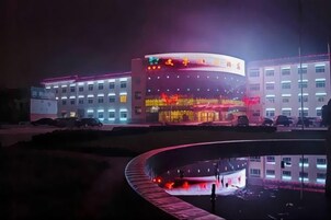 Un edificio de varios pisos, con fachada curva y un elemento acuático reflectante al frente.