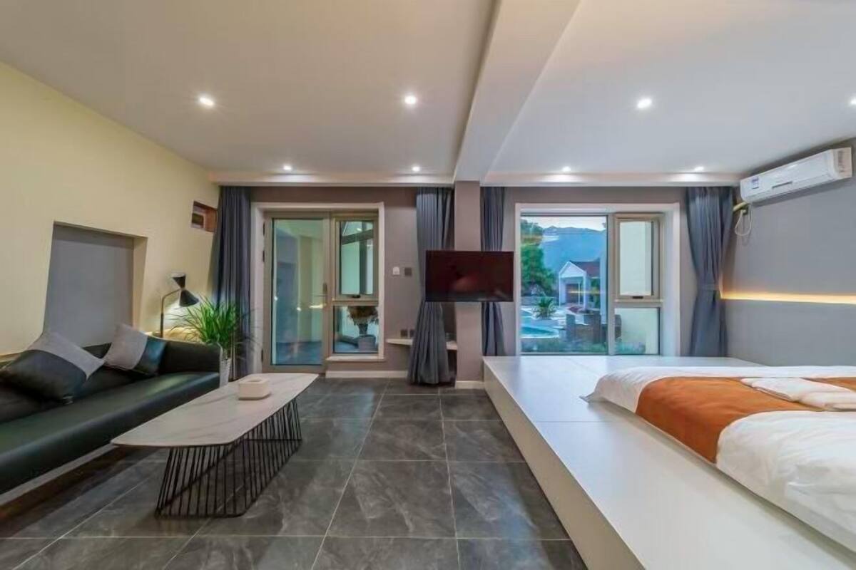 Quarto de hotel com sofá, cama, televisão e vista para uma piscina.