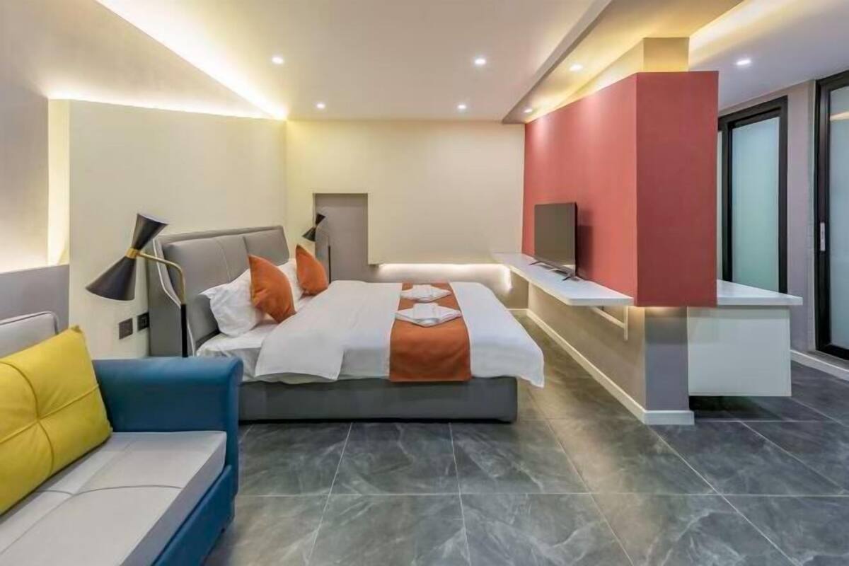 Quarto de hotel moderno com cama, escrivaninha, televisão e sofá.