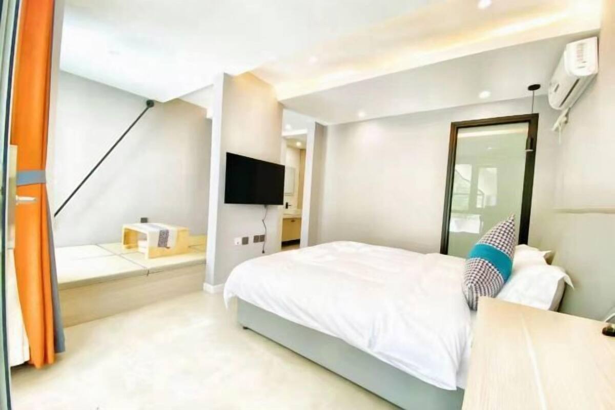 Quarto de hotel moderno com cama, televisão de tela plana, mesinha e janela com cortinas.