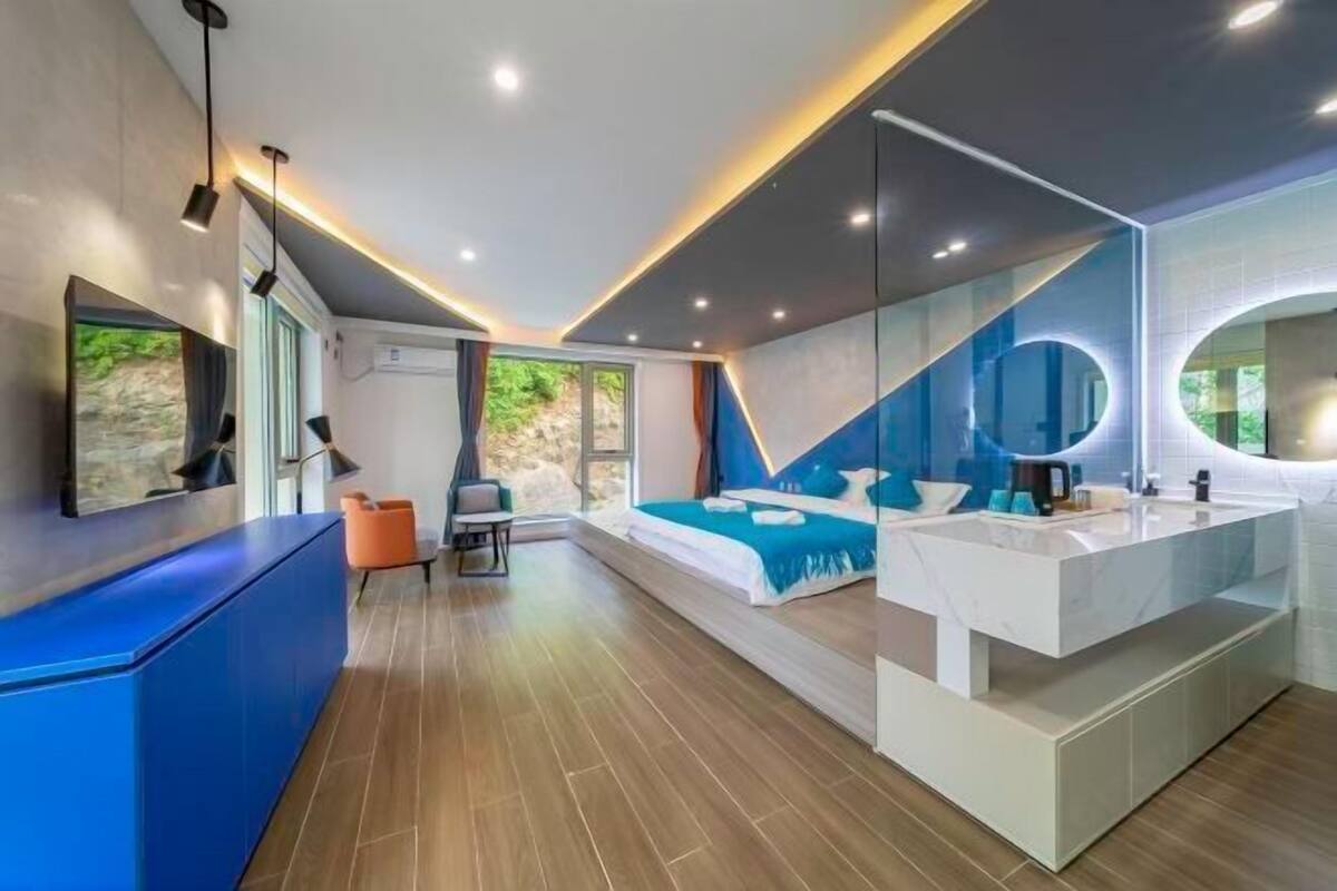 Quarto de hotel moderno com cama grande, banheiro privativo com toucador, área de estar e uma janela ampla.