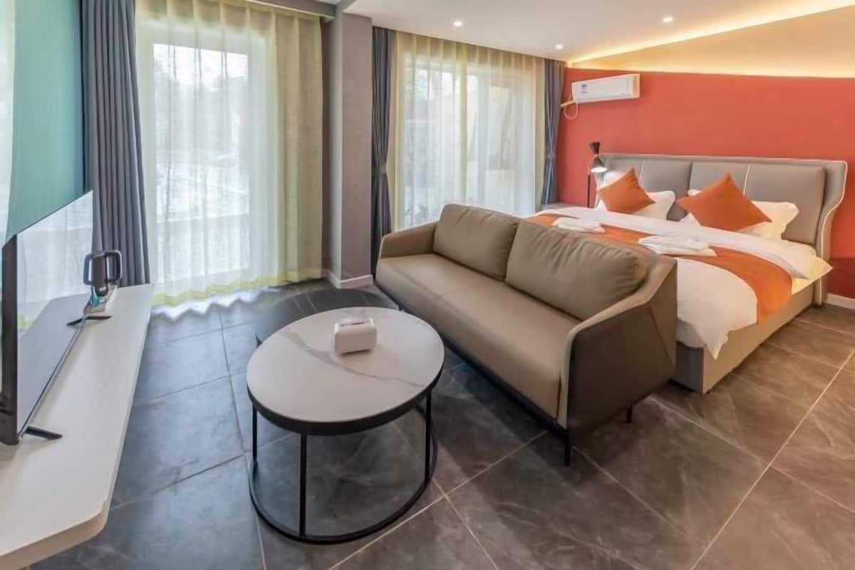 Quarto de hotel com cama, sofá, mesa redonda pequena e televisão.