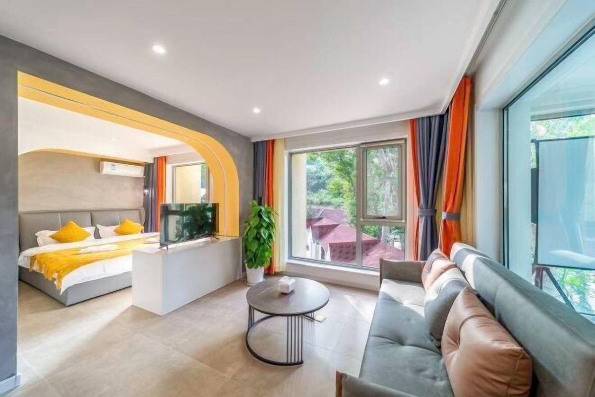 Quarto de hotel moderno com cama, sofá, televisão e vista para área verde.