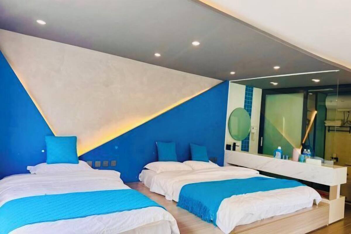 Quarto de hotel moderno com duas camas, um espelho grande e piso de madeira.