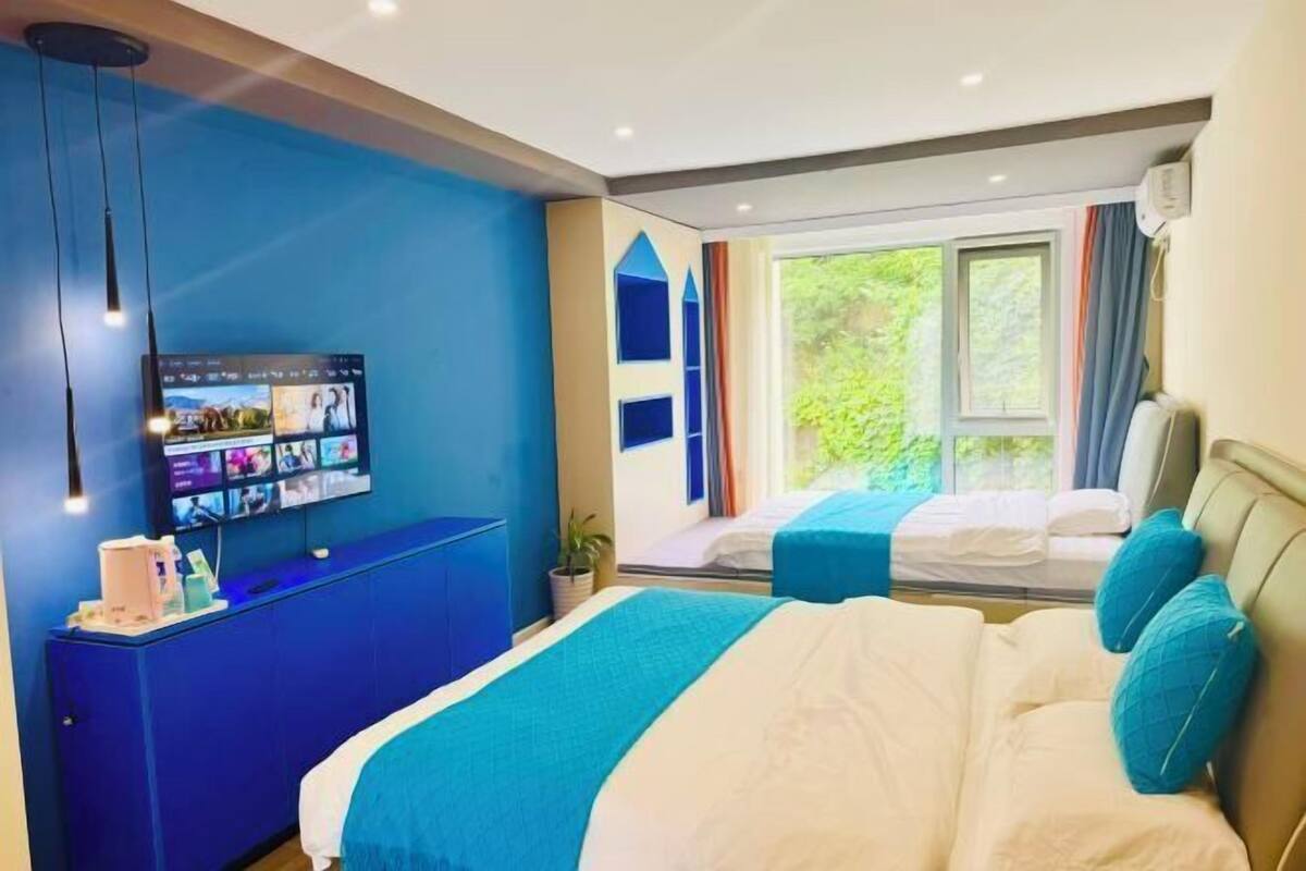 Quarto de hotel moderno com uma cama grande, uma escrivaninha com computador e uma janela com vista para o verde.