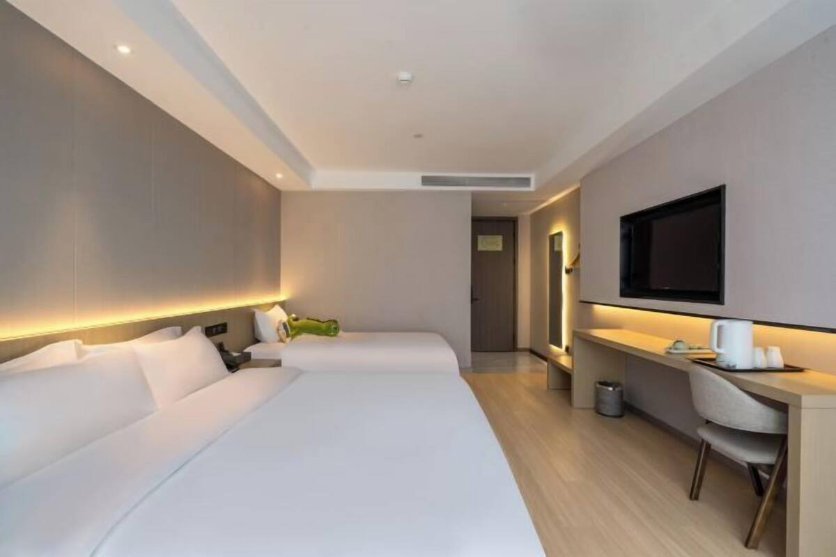 A modern hotel room with two beds, a desk, a flat-screen TV, and a small seating area.
