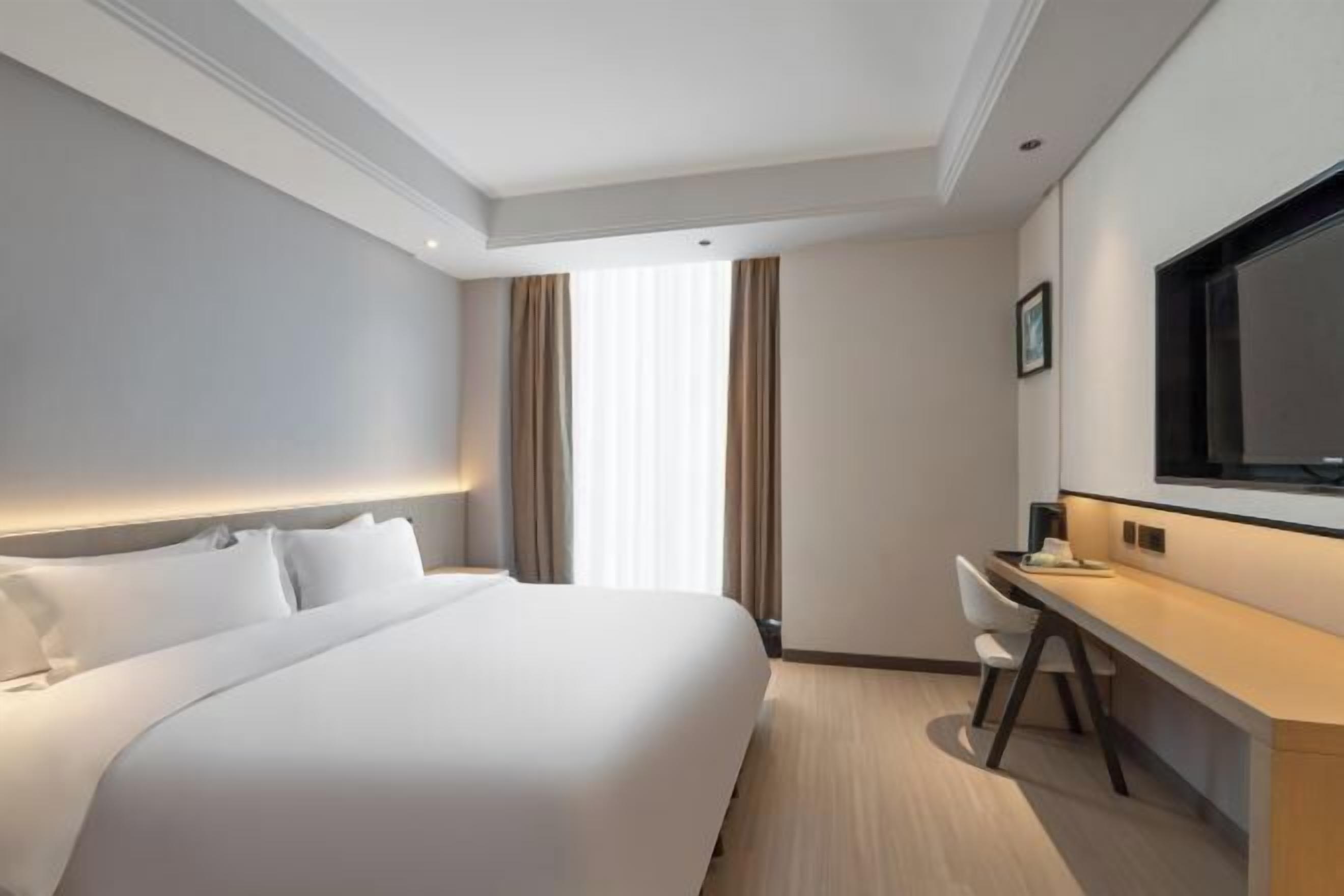 A hotel room with a bed, a desk, a chair, and a television.