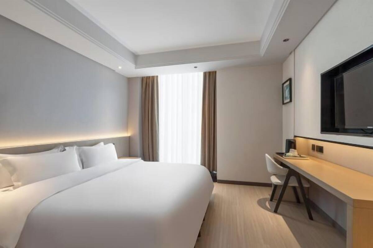 A hotel room with a bed, a desk, a chair, and a television.