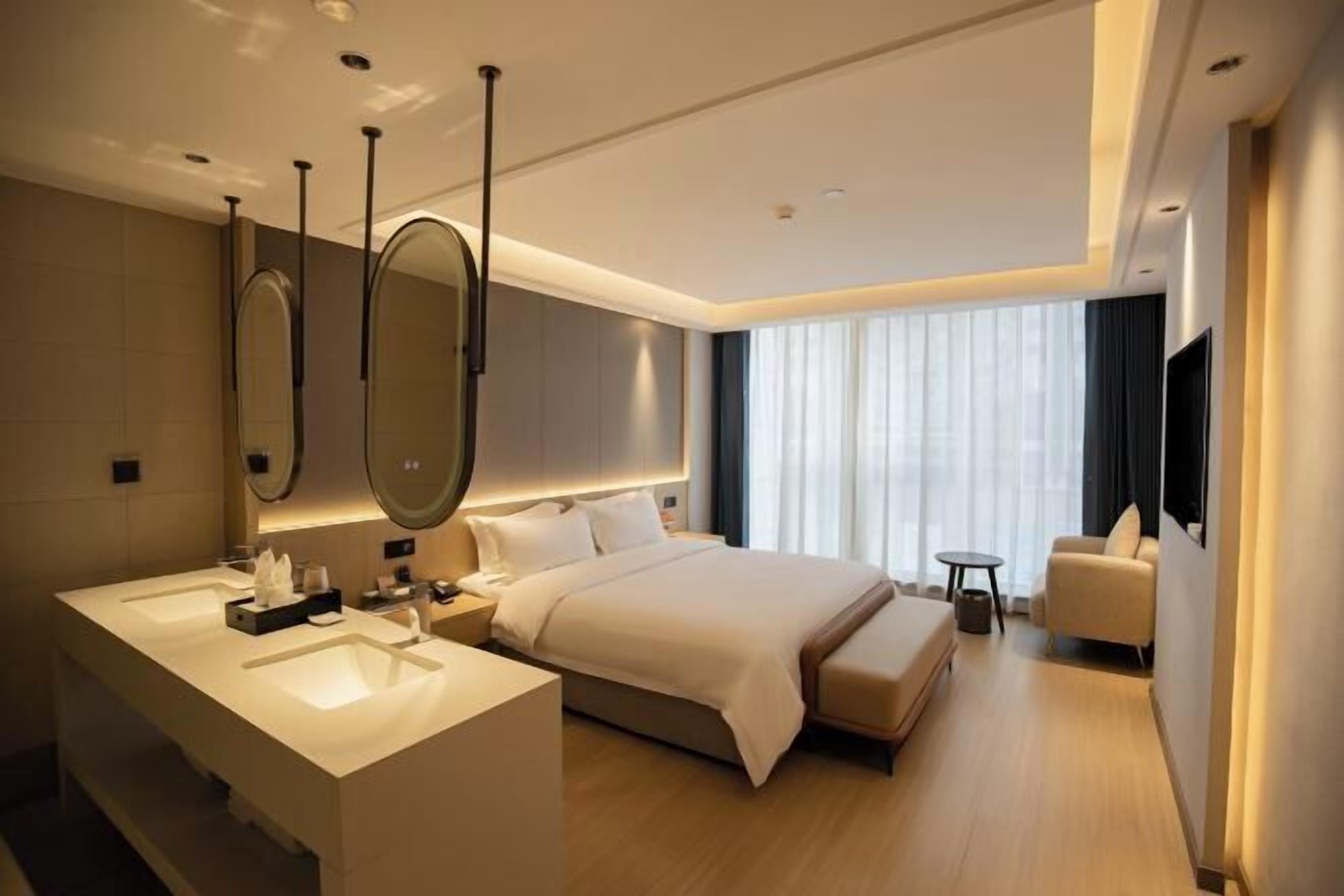 A modern hotel room with a large bed, a separate bathroom with a vanity, a small round table, and a chair.